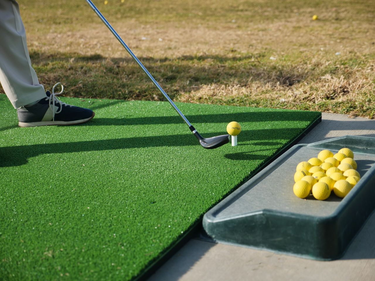 Close-up of a golfer practicing on artificial turf with golf balls on tee.