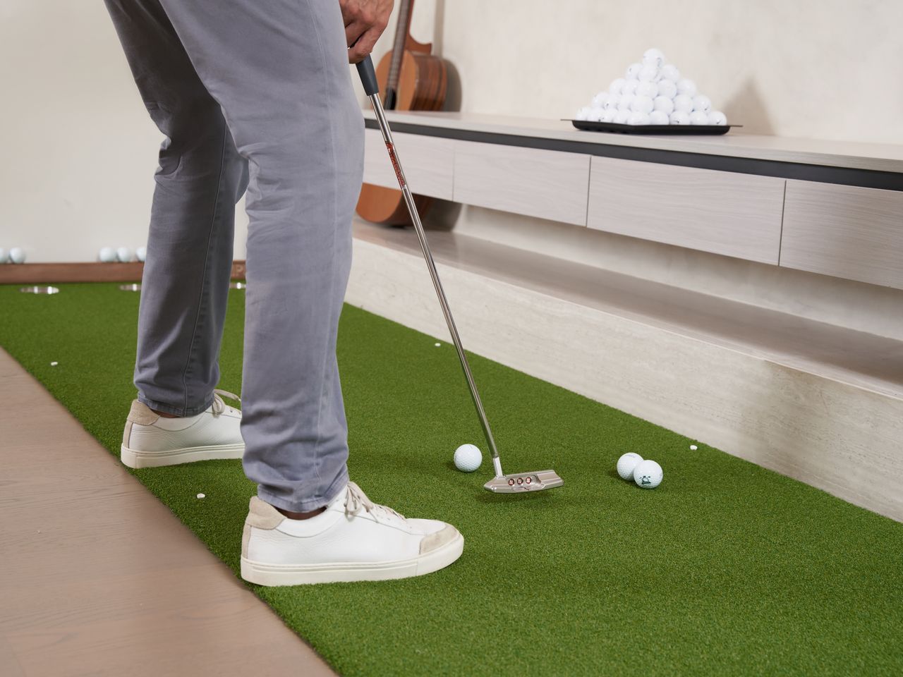 A golfer practicing putting on an indoor synthetic golf mat with golf balls and a club.